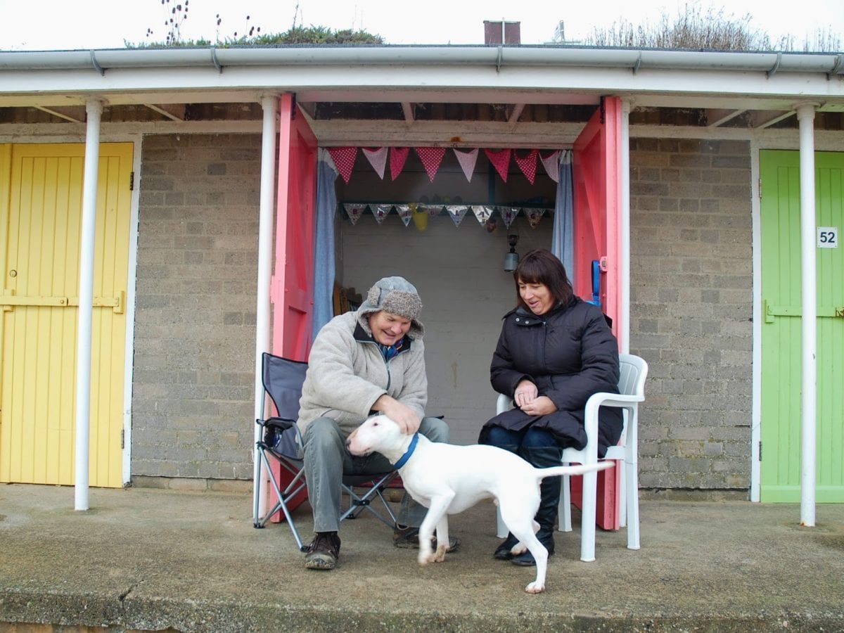 A couple and their dog outside their beach hut